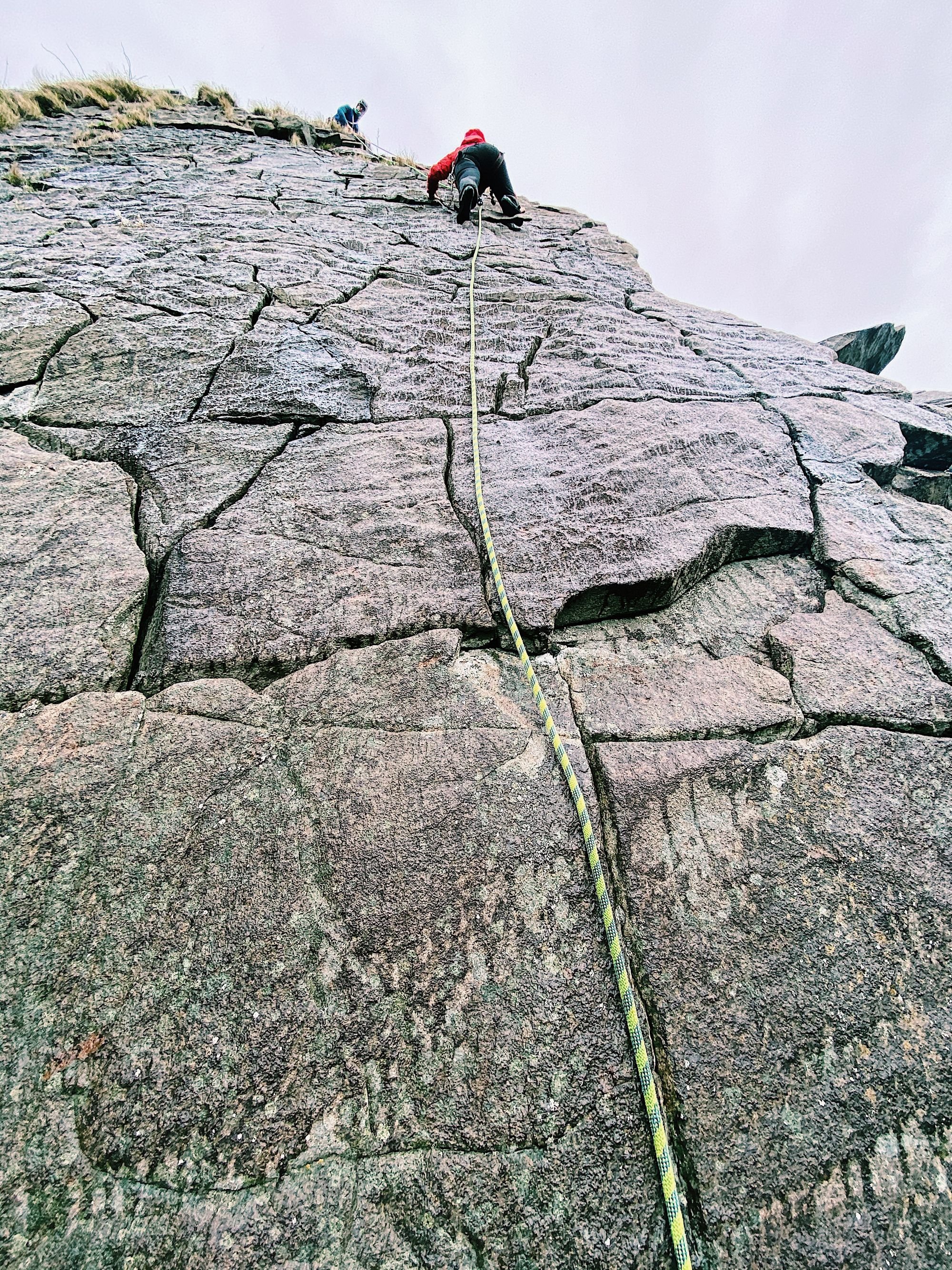 A climber ascends a vertical rock face on the Isle of Skye.