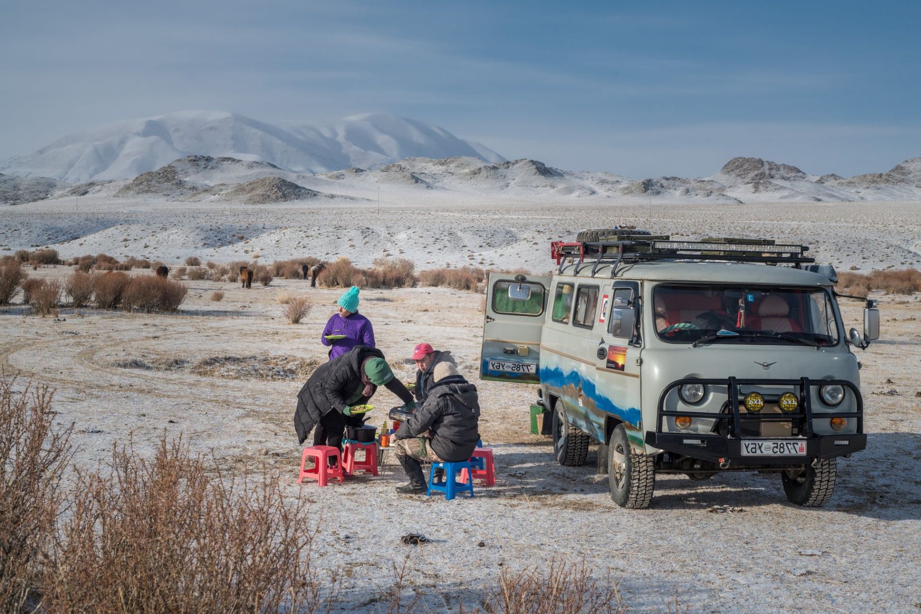People eating lunch in the Mongolian desert, next to a van 