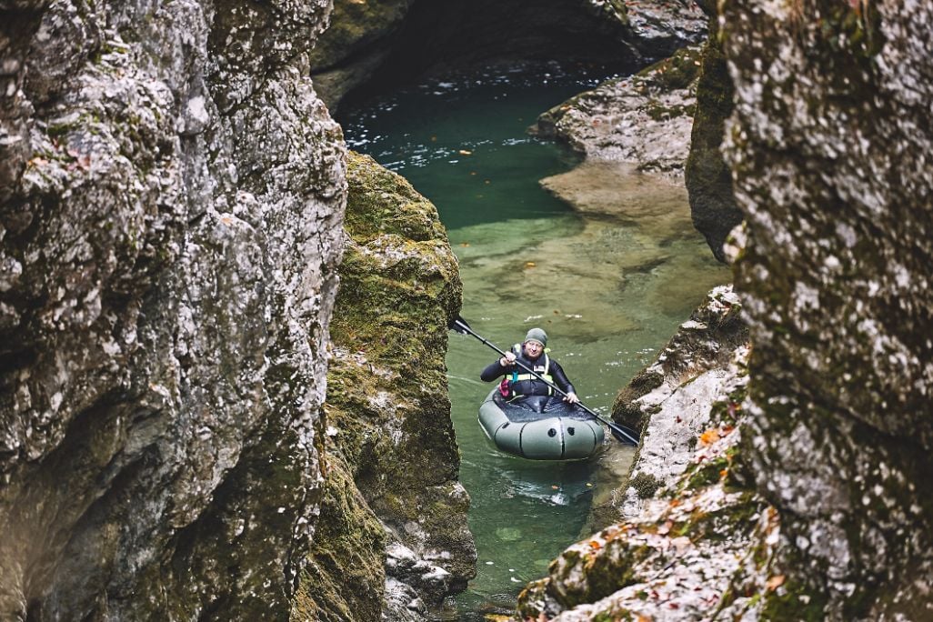 A packrafter wearing a personal floatation device and spray deck, approaching a gorge