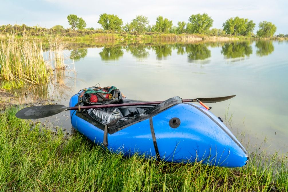 A packraft, ready to board, on the edge of a lake