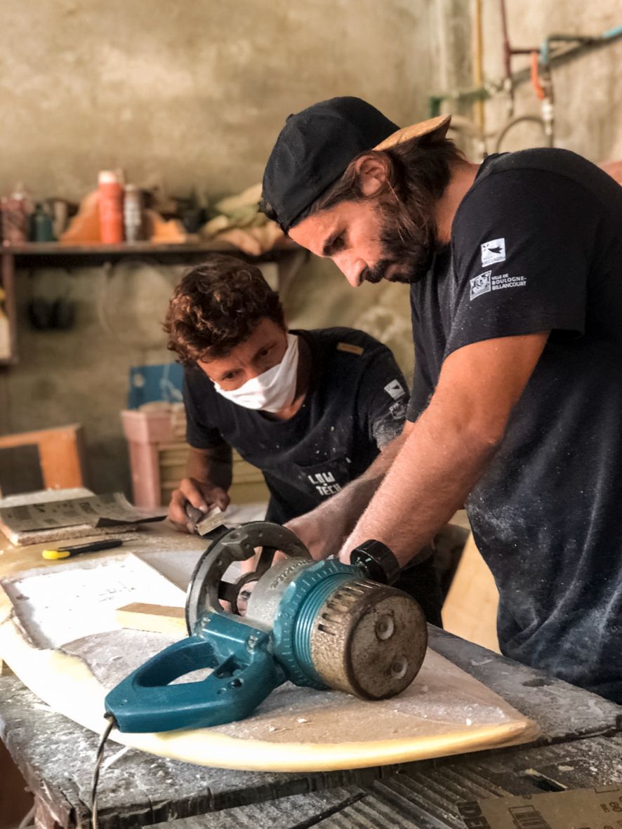 Damien Castera and friend Coco repairing a surfboard.