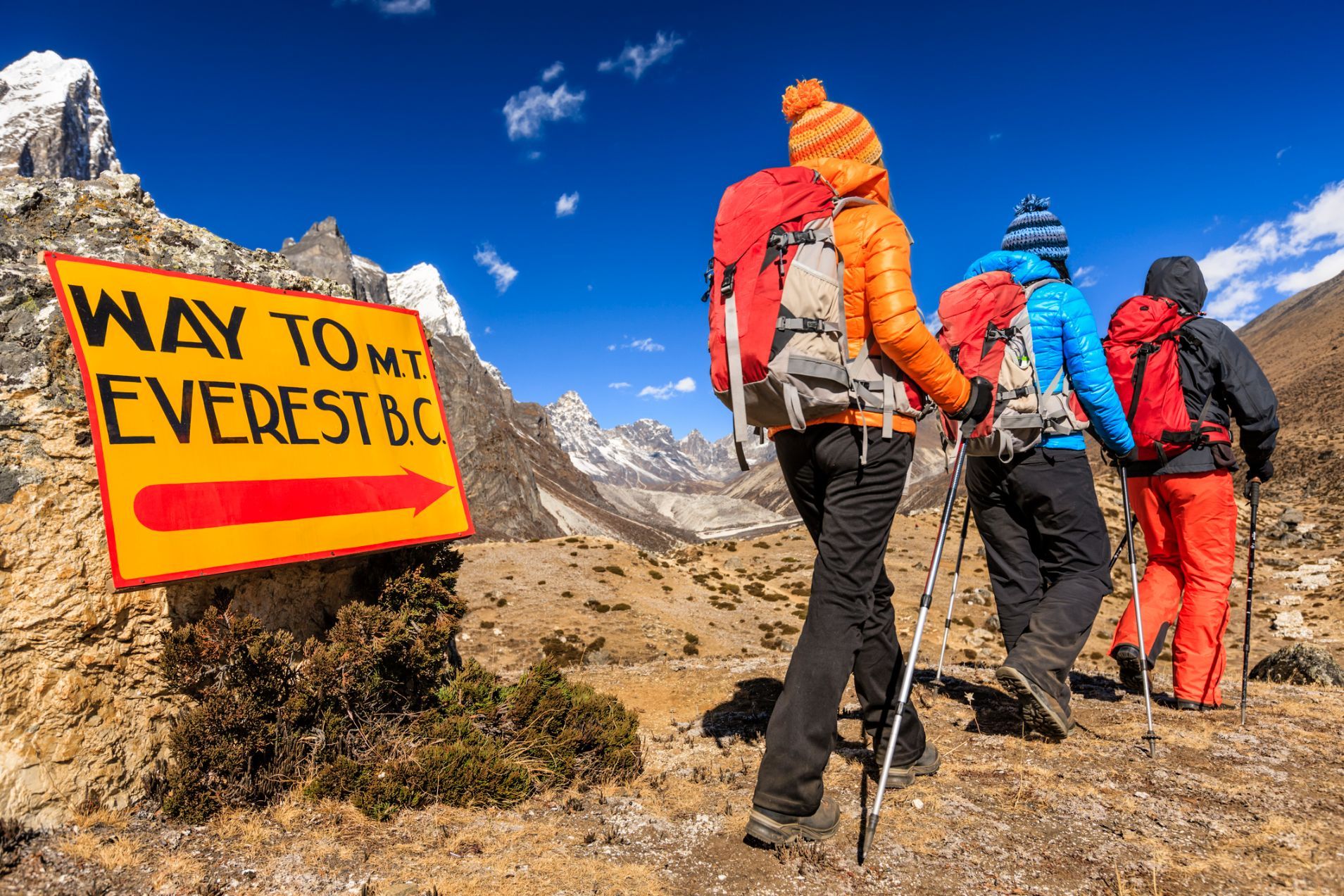 The sign for Everest Base Camp, and three hikers walking in the direction of its arrow.