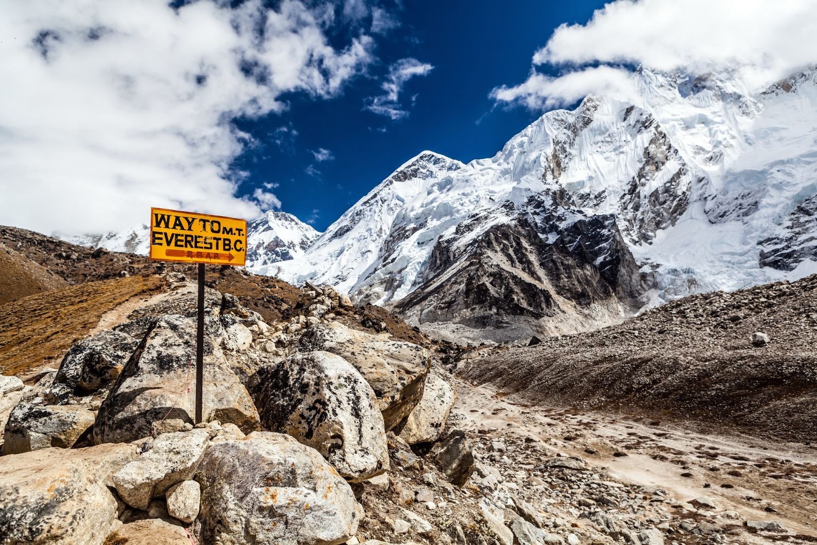 A sign indicating the direction to Everest Base Camp, with a backdrop of the Himalayas.