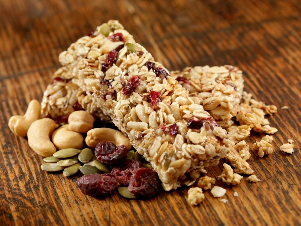 A close up of hiking snacks including a granola bar, nuts, seeds and dried cranberries.