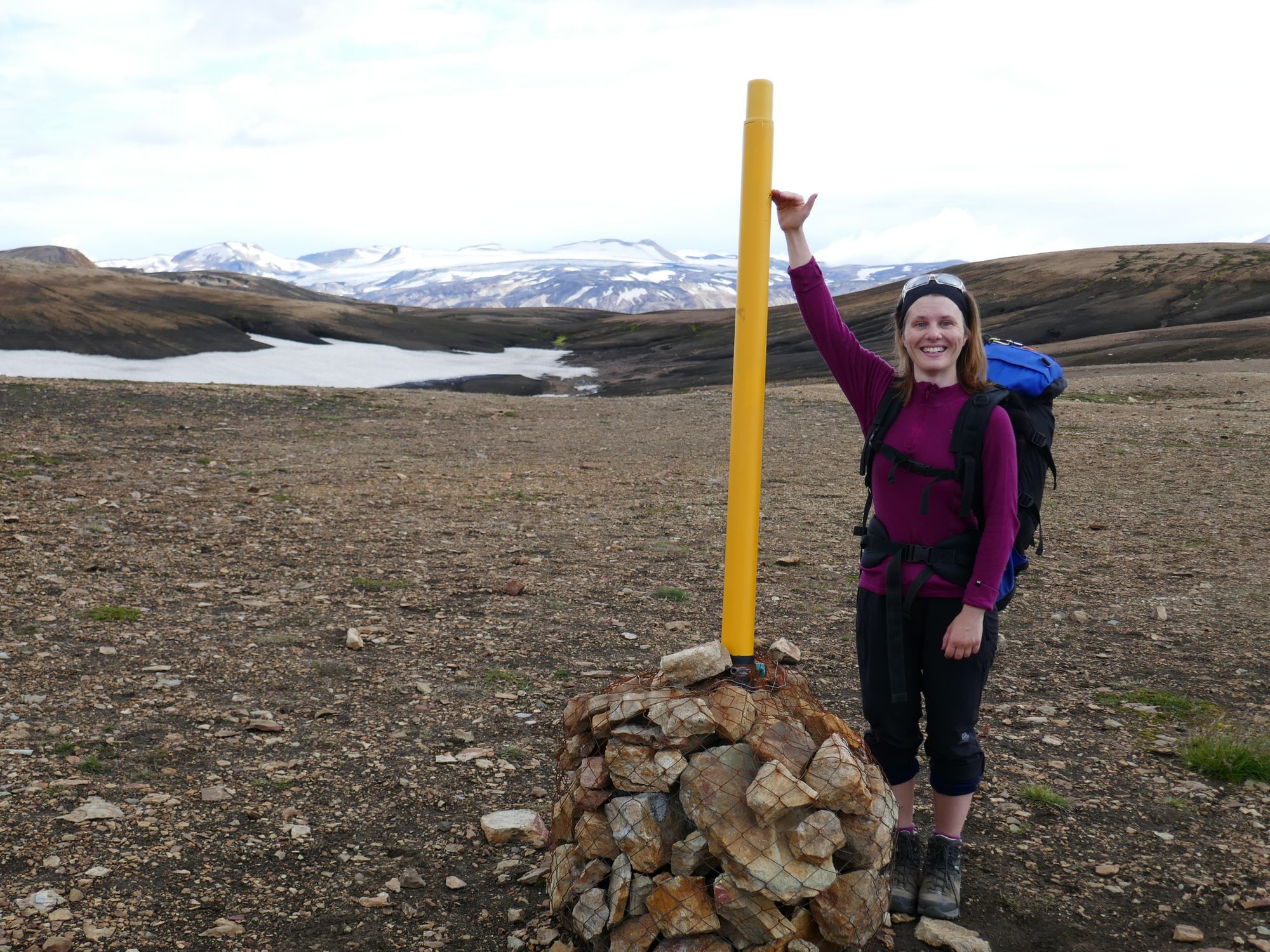 A woman hiker poses behind a snow pole on the Laugavegur Trail, in Iceland.
