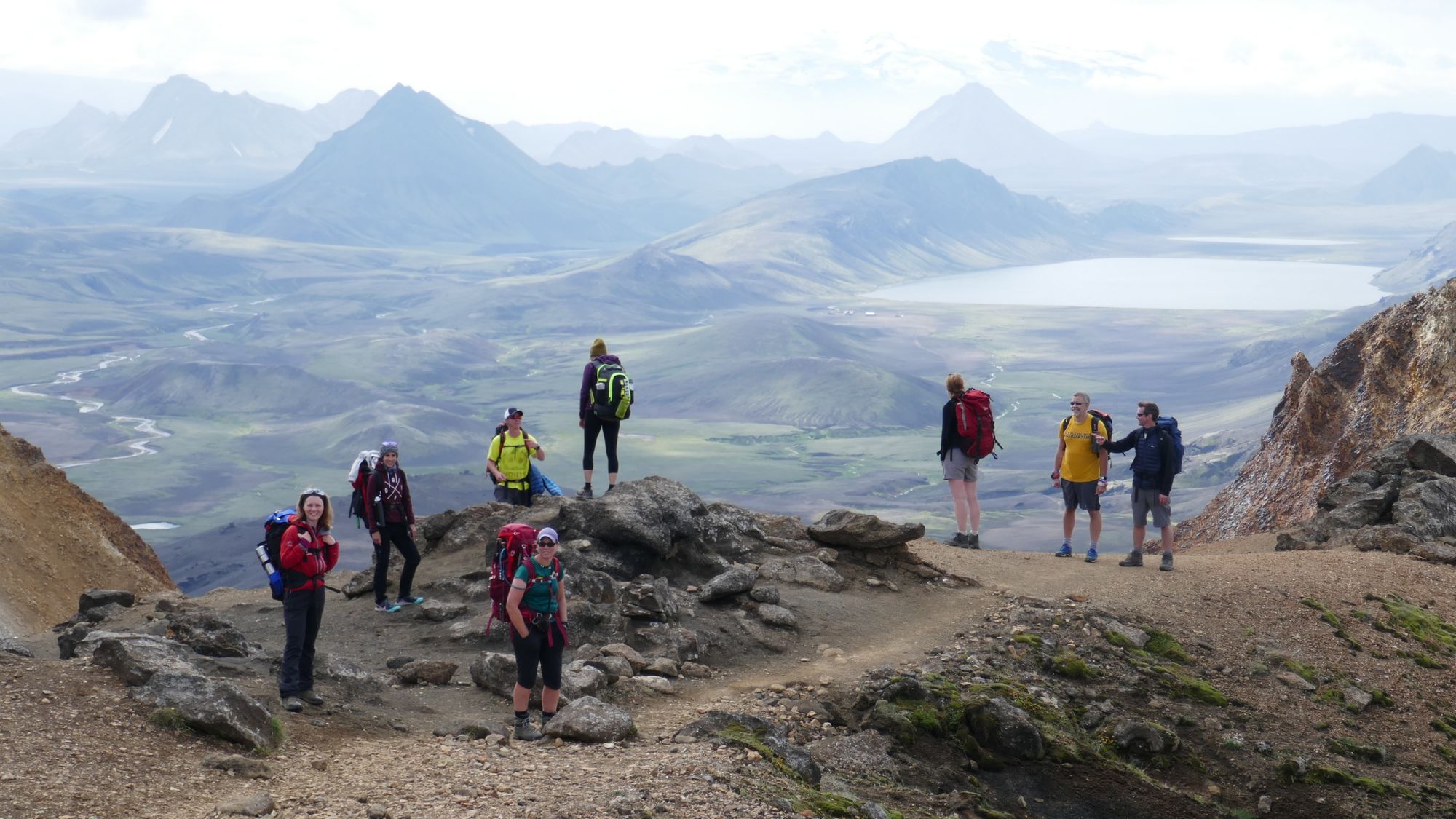 Hikers standing on a plateau looking down over the volcanic landscape of Álftavatn in Iceland.