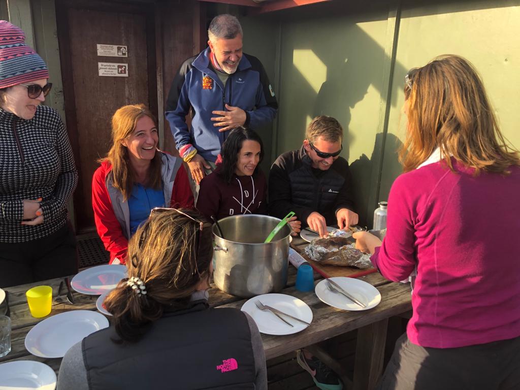 A hiking group eating a meal on a picnic bench.