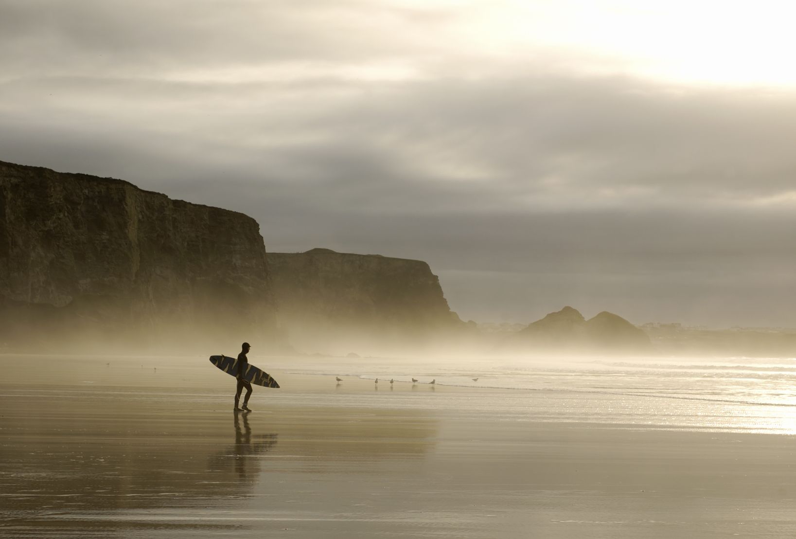 A surfer walking through the winter morning mist to hit the waves on a Cornish beach. Photo: Getty