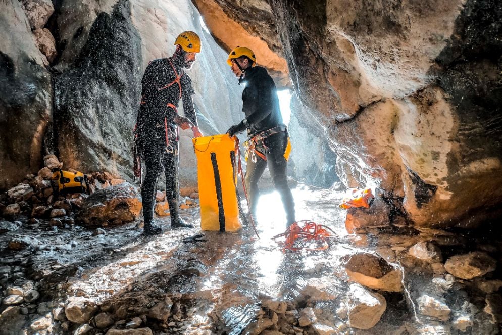 Two canyoners inside a cave, packing their gear into a dry bag.