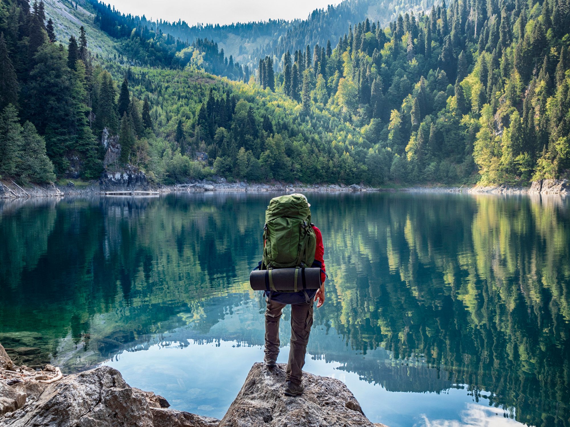 A hiker with a large backpack looking out at a lake.
