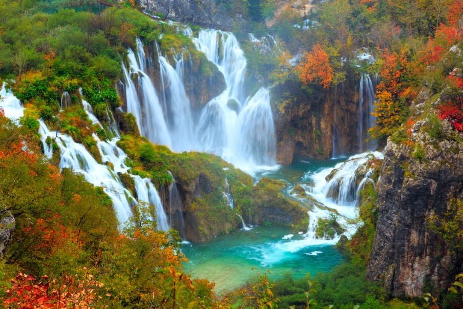 A view of waterfalls in Plitvice Lakes National Park, surrounded by autumn foliage.