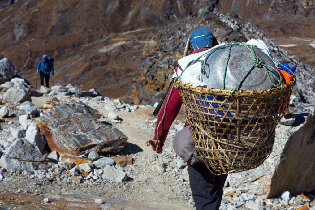 A mountain porter carries a wicker basket of cooking equipment.