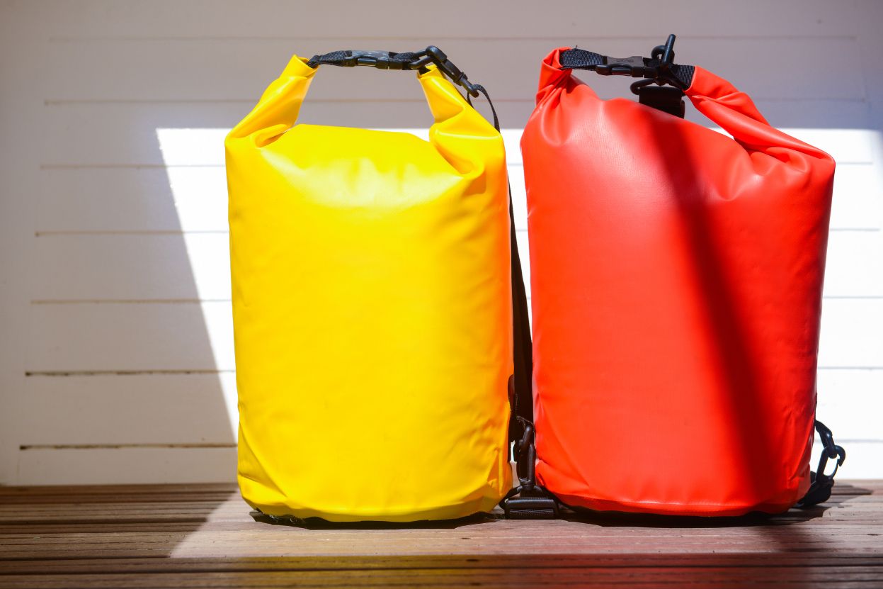 Two full dry bags leaning against a white wooden wall.