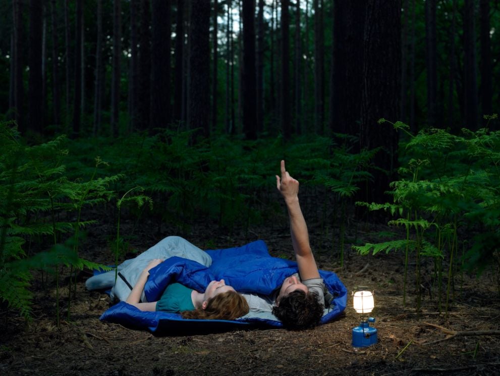 Two people sleep outdoors in a two-person tent, under the stars.