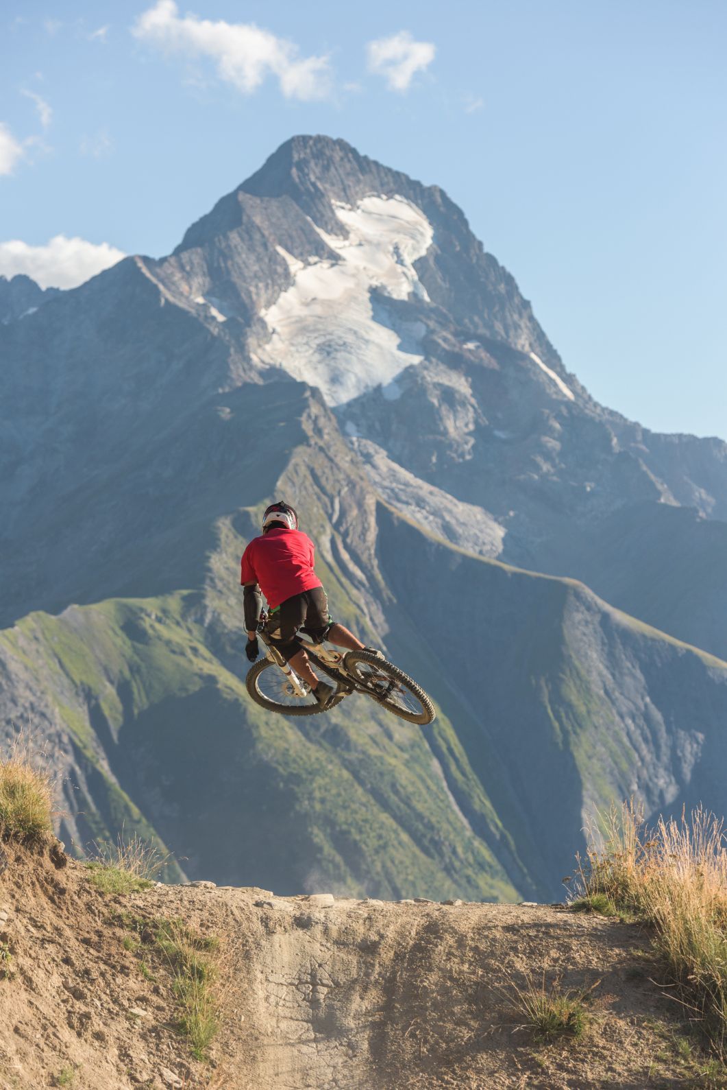 A mountain biker jumping in the air, with Alpe d'Huez and Les Deux Alpes in the background.