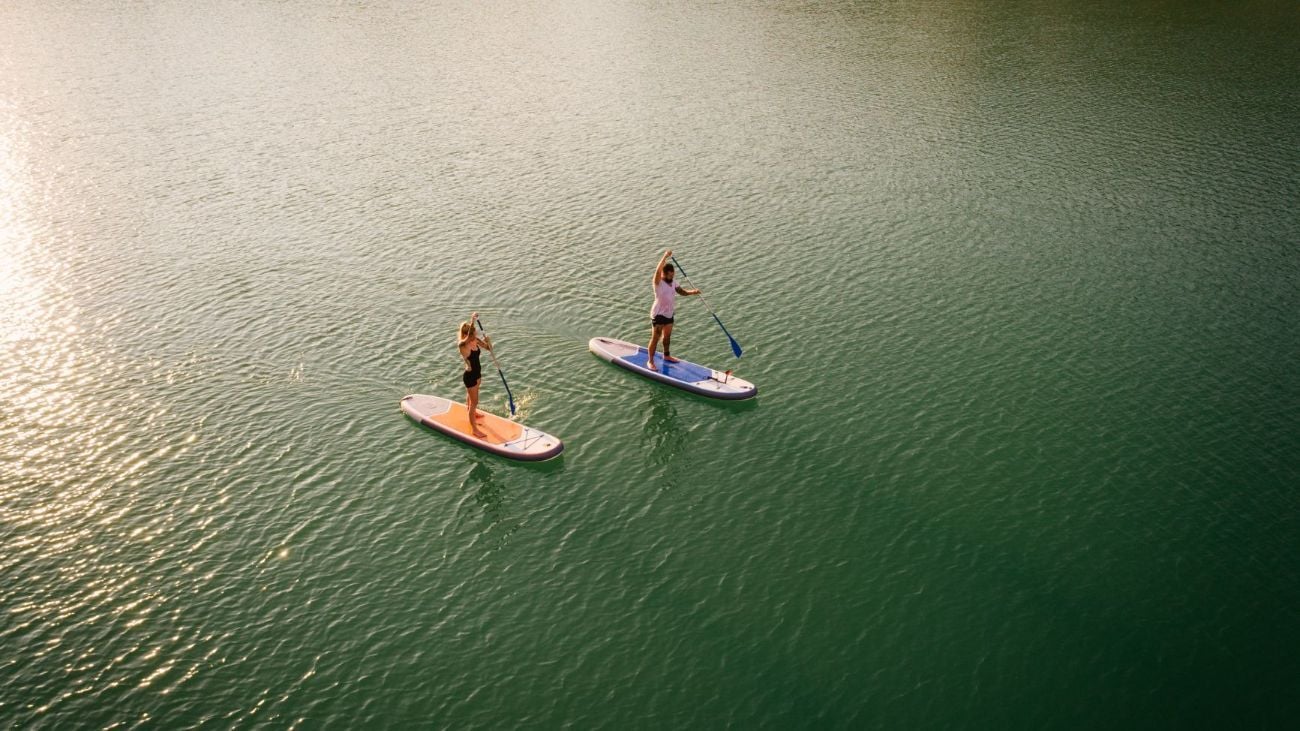 Two stand-up paddleboarders wade through a lake.