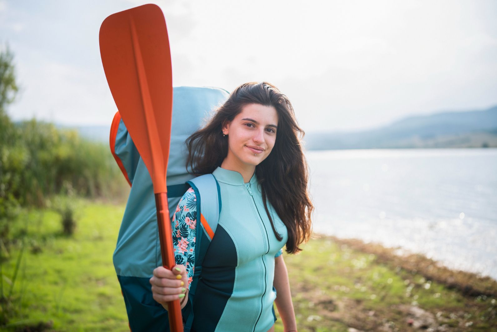 A woman with a rucksack containing a deflated, inflatable stand-up paddleboard and accessories, packed away.