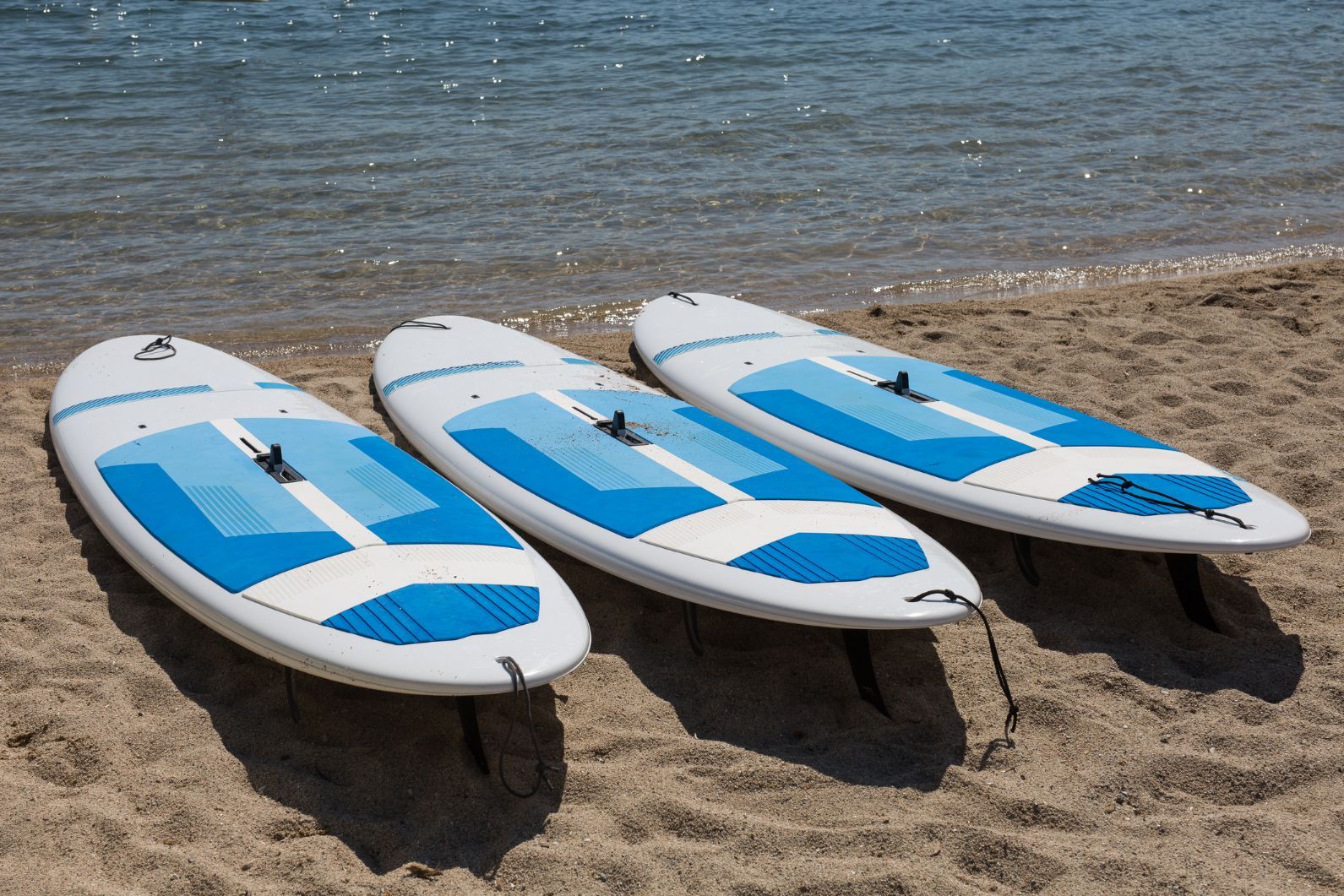 Three stand-up paddleboards lie on a beach, waiting to be used.