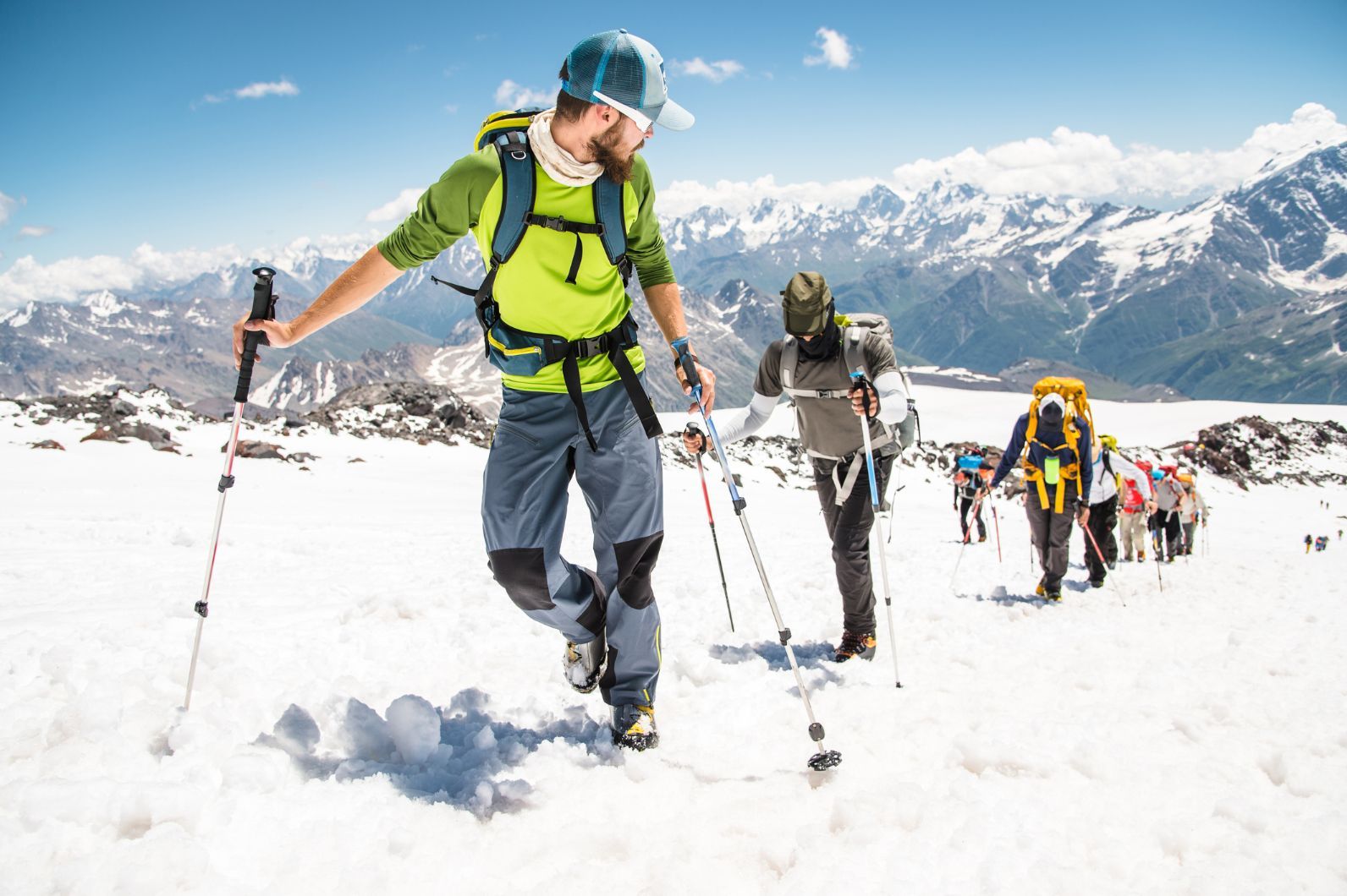 A group of hikers makes their way up a snowy mountain, following in a long line.