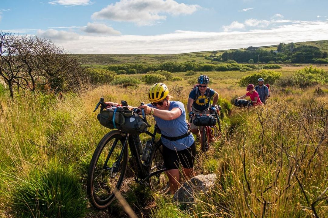 Cyclists pushing their bikes up an overgrown track