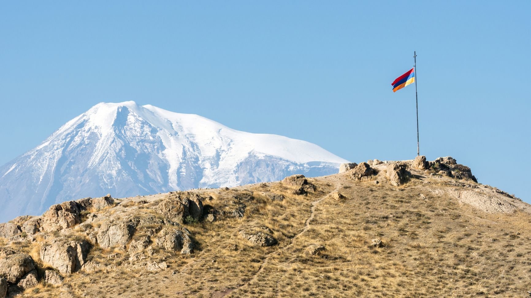 A view of the snowy peak of Mount Ararat in the background, with the Armenian flag in the foreground.