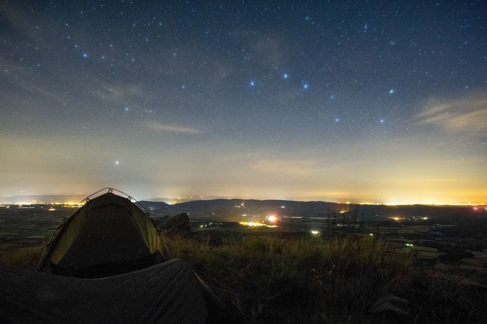 A solitary tent at night - the big dipper constellation is clearly visible in the sky above.