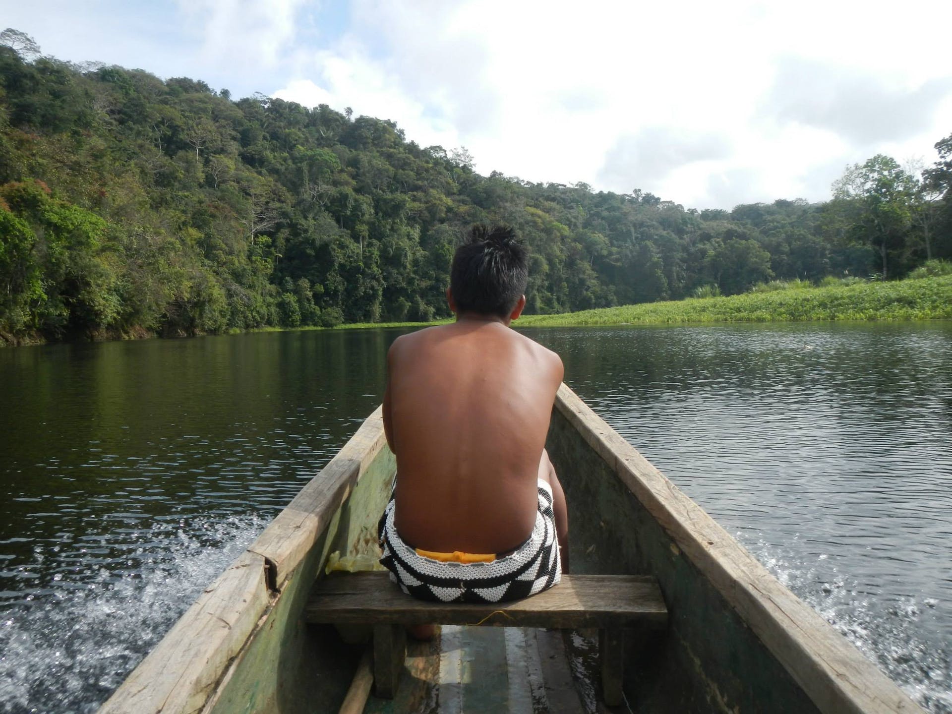 An indigenous guide working with Javier leads a team up the river, flanked by lush green forests.