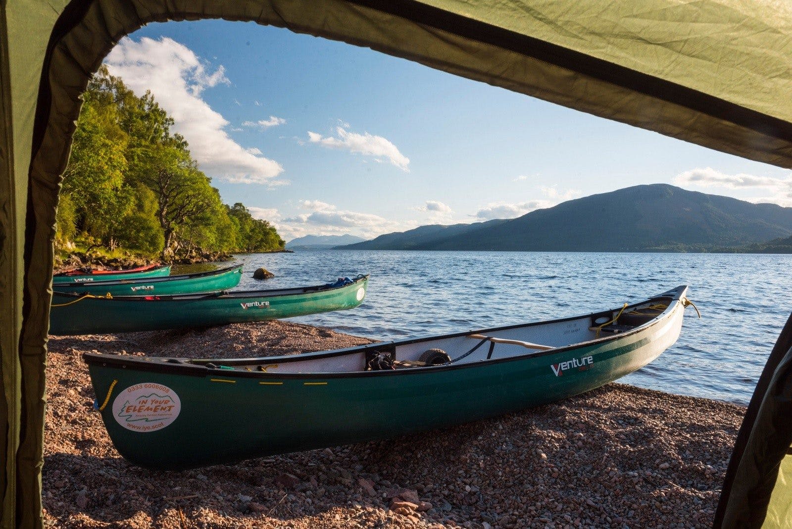 Four canoes on the rocky shore of a Scottish loch, viewed through a tent flap.