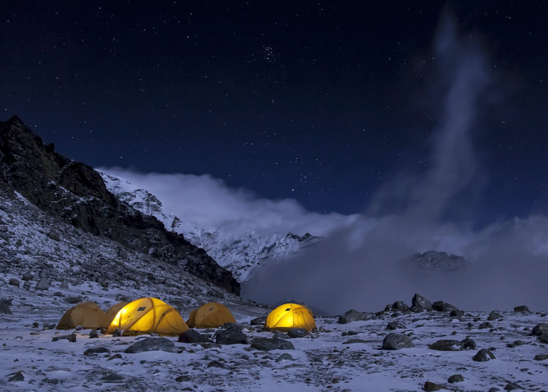 Illuminated tents surrounded by snow and ice, a wild campsite on Yala Peak in Nepal.