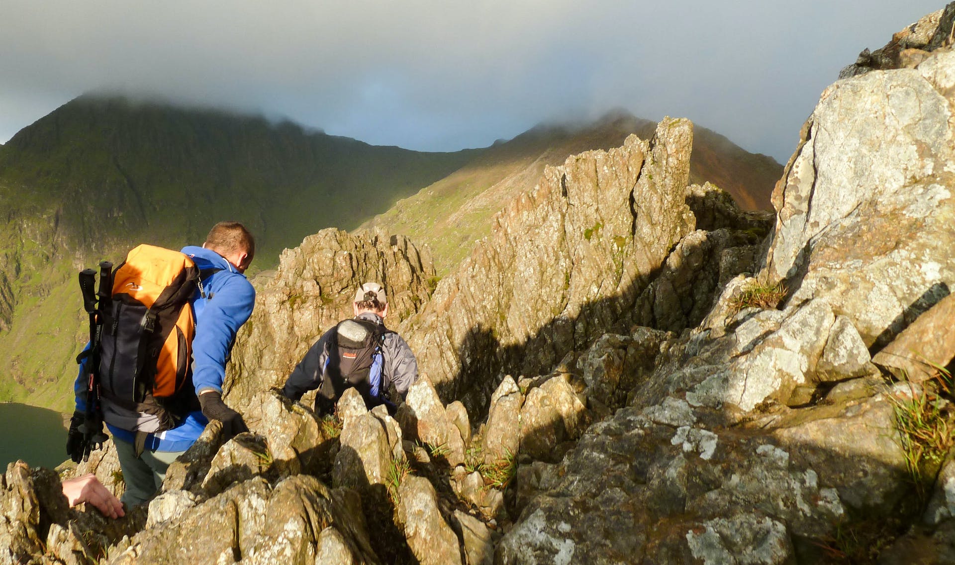 Two hikers scramble over a rocky ridge in Snowdonia National Park.