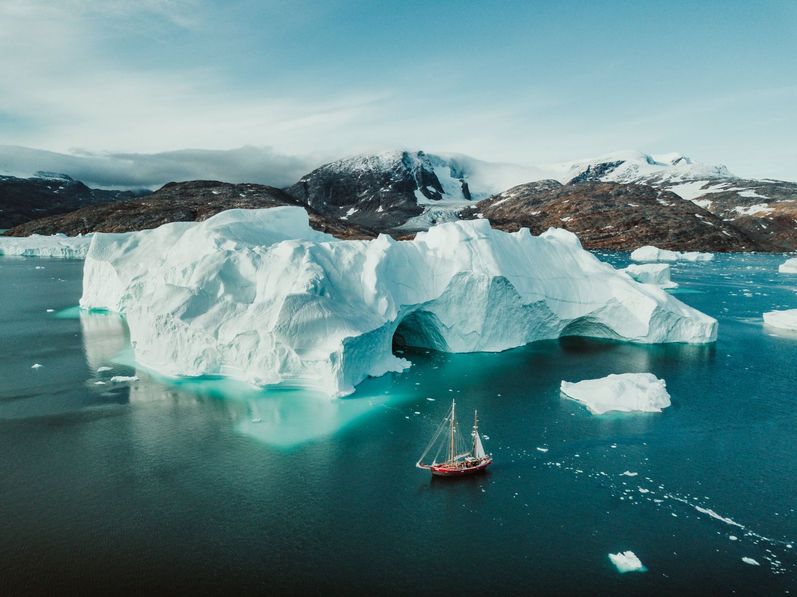 A tall ship sails past an iceberg in Greenland.