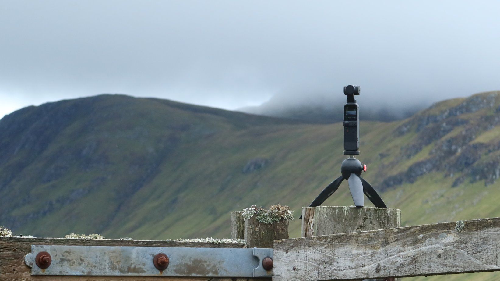 The filming process with a tripod set up on a fence, and the background of mountains.