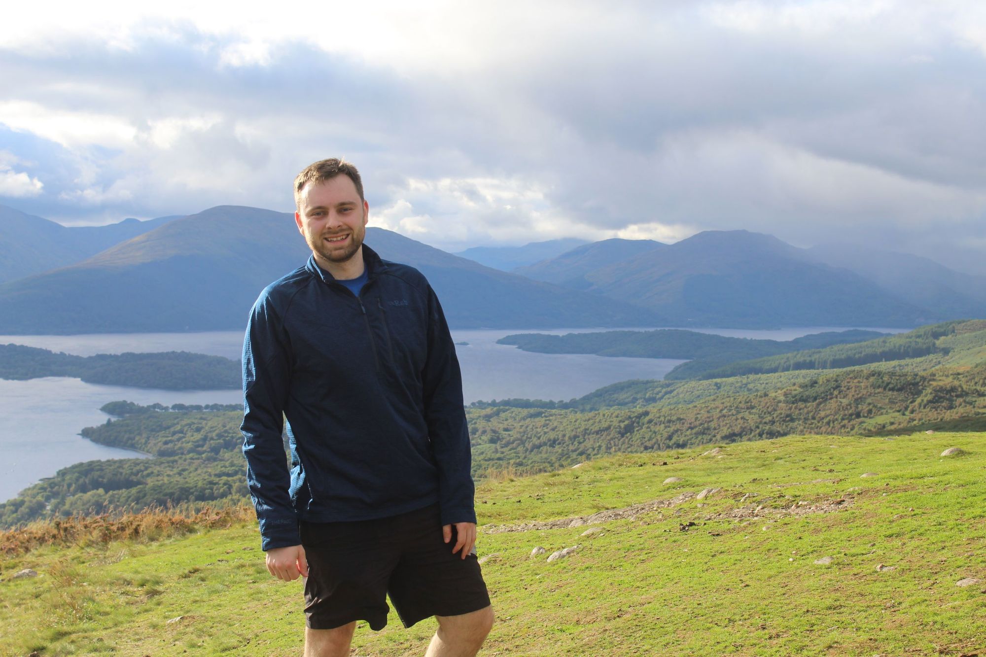 A man posing at the top of Conic Hill, with Loch Lomond in the background.