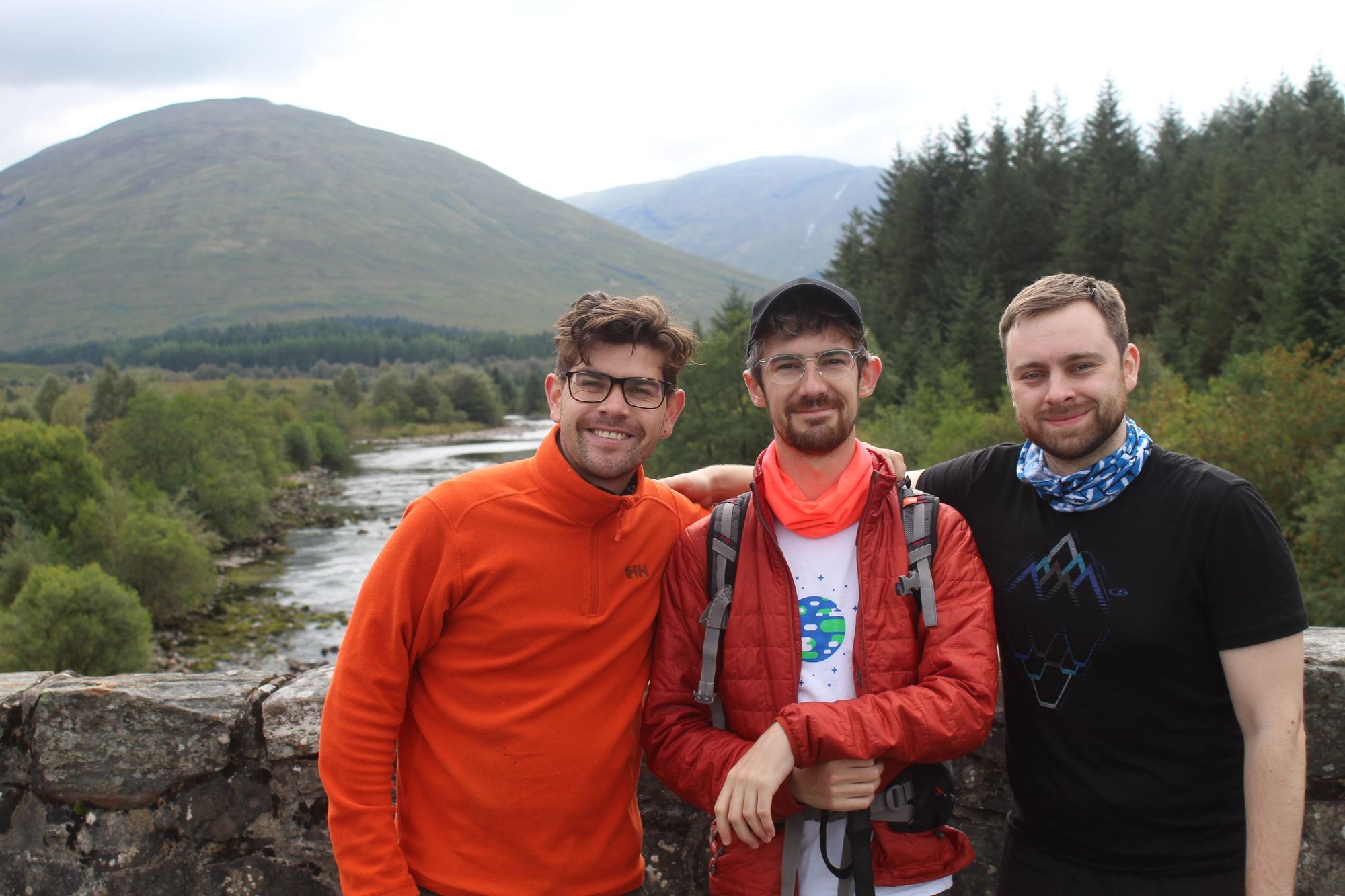 Three hikers pose on the stone bridge over the River Orchy in Scotland.