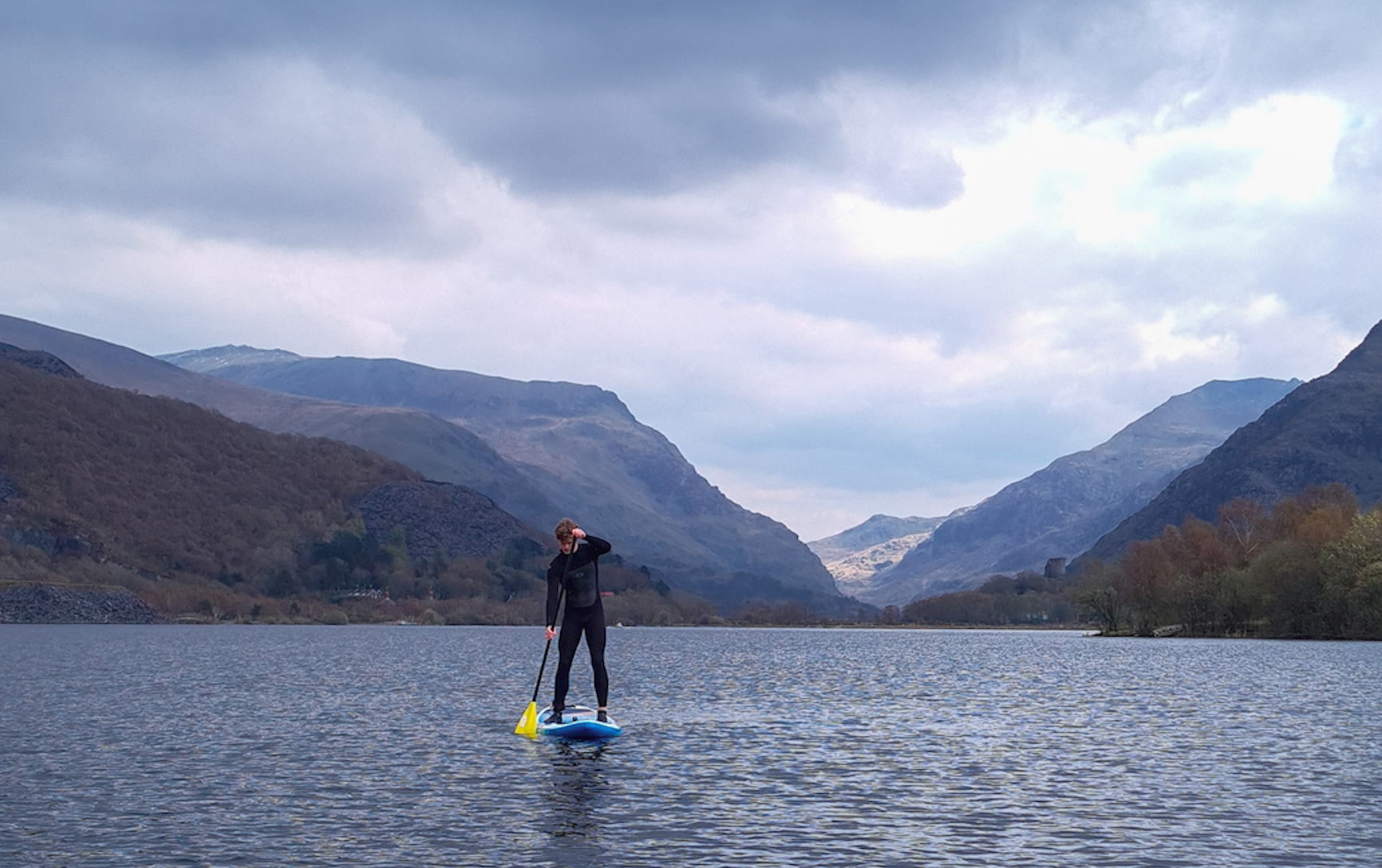 A man stand-up paddleboarding on Llyn Dinas, beneath Snowdon in Wales.