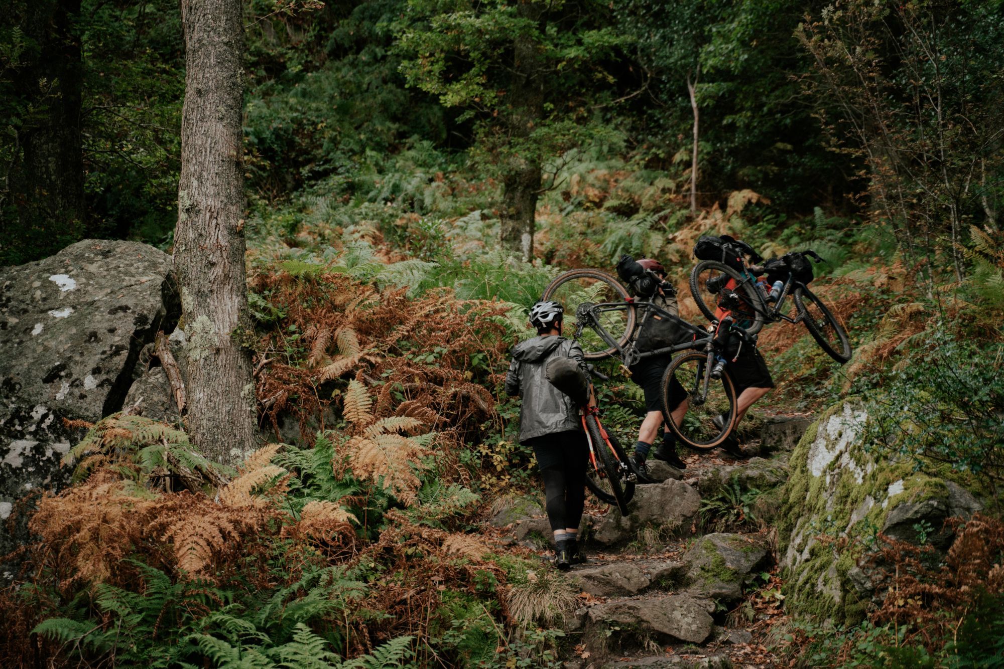 Lee Craigie, Alice Lemkes and Phillipa Battye of the Adventure Syndicate, carrying their bikes up a rocky hill.