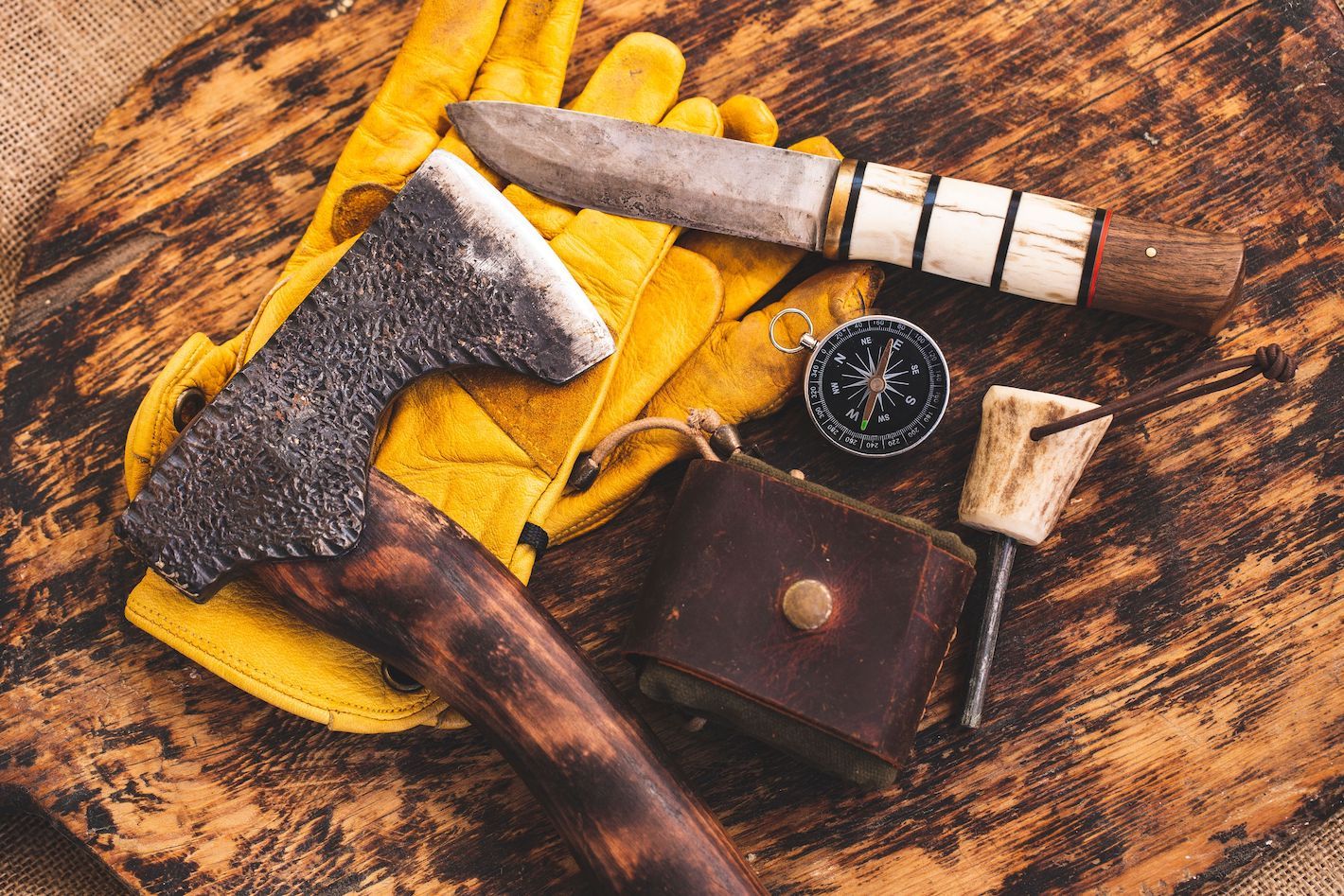 Bushcraft tools including an axe, a knife, a whetstone, a compass and a ferro rod.