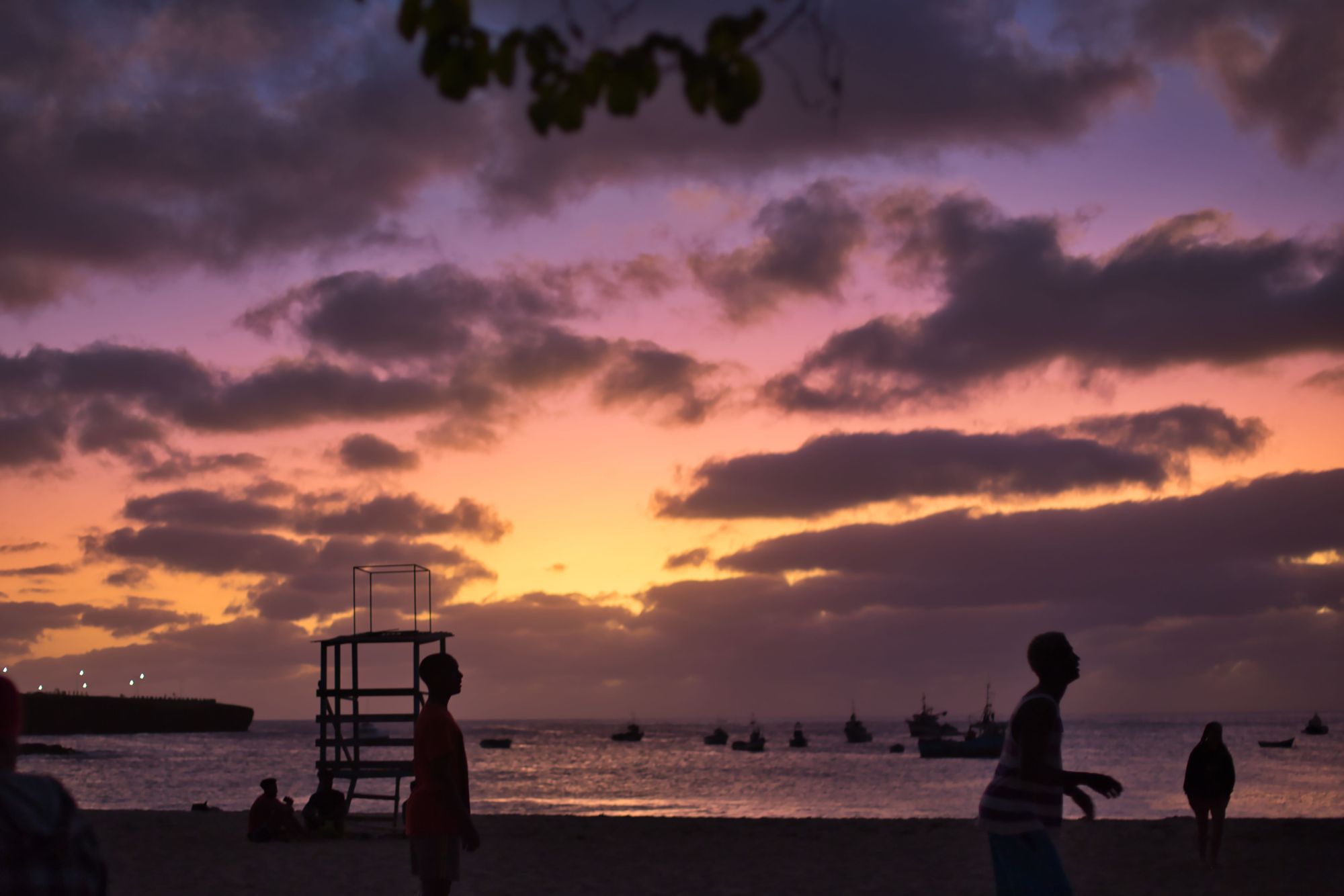 People on the beach at sunset, with boats in the sea behind them in Cape Verde