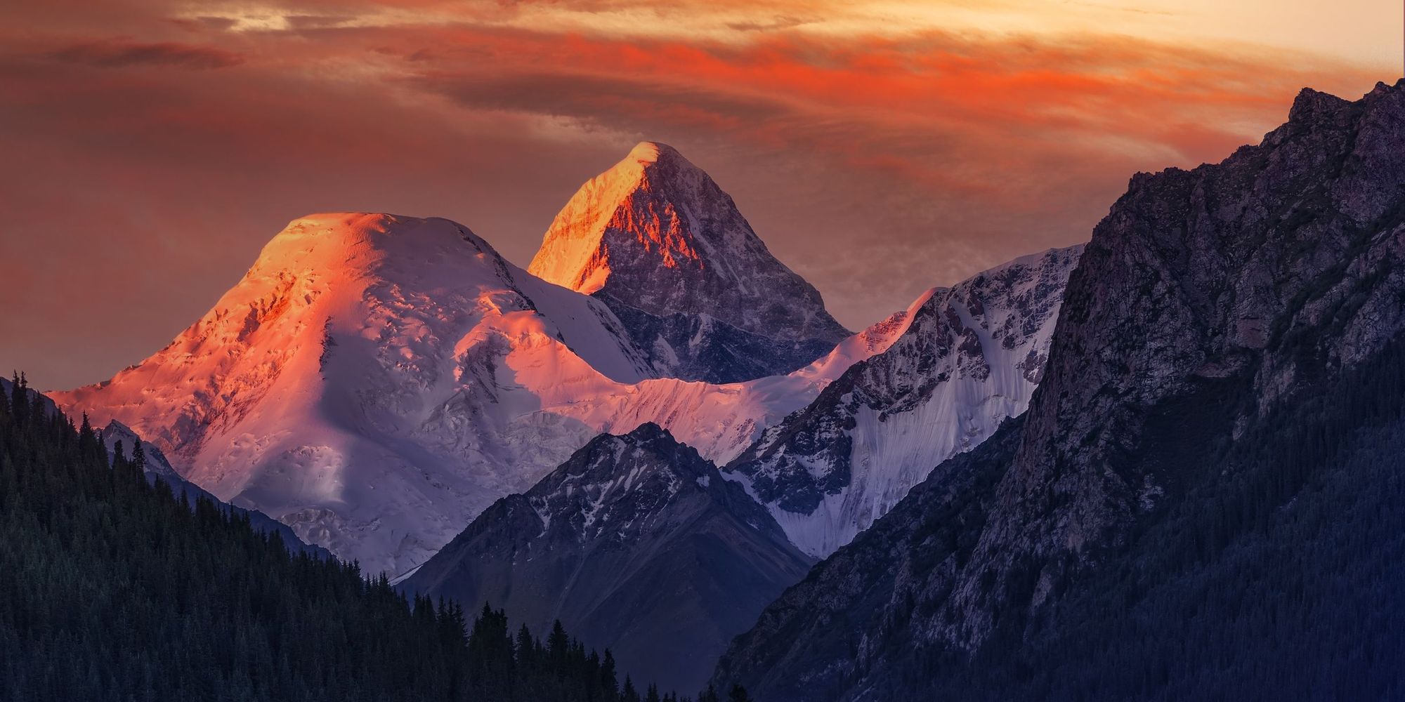 The snowcapped summit of Khan Tengri reflecting orange light at sunrise.
