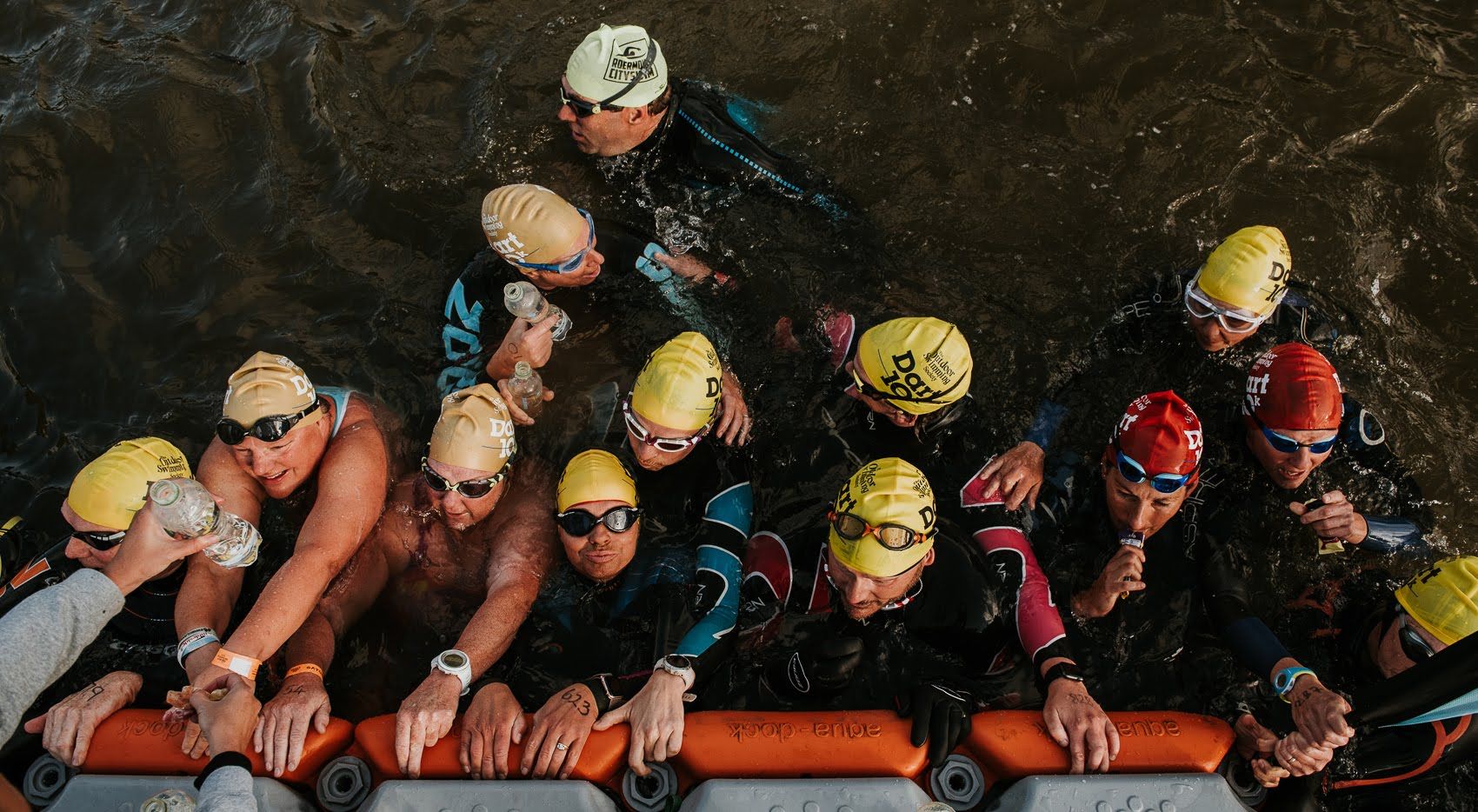 Swimmers wearing colourful hats, holding onto a refreshment station on the Dart 10k race.