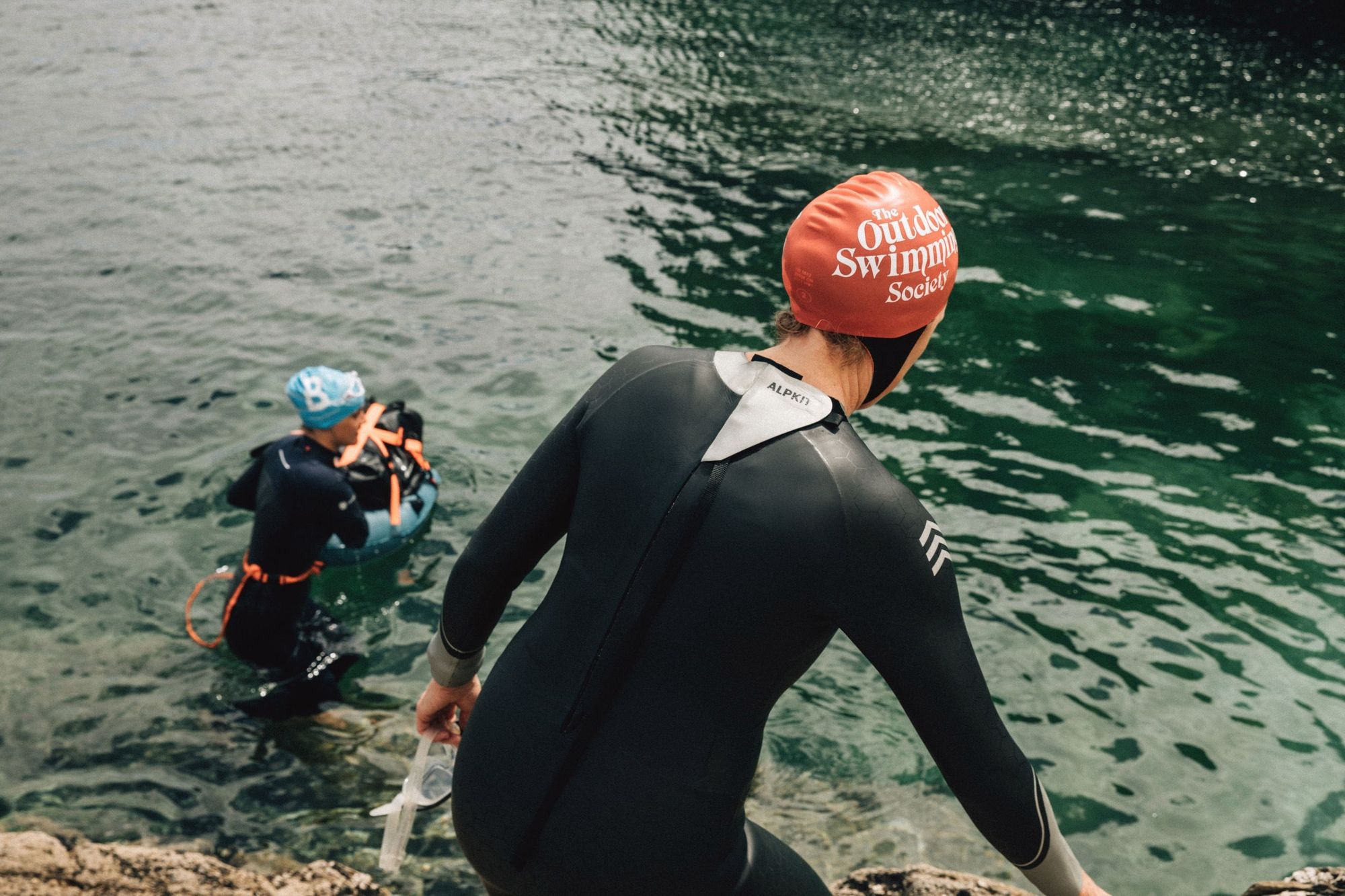 Women swimmers entering the ocean, wearing wetsuits.