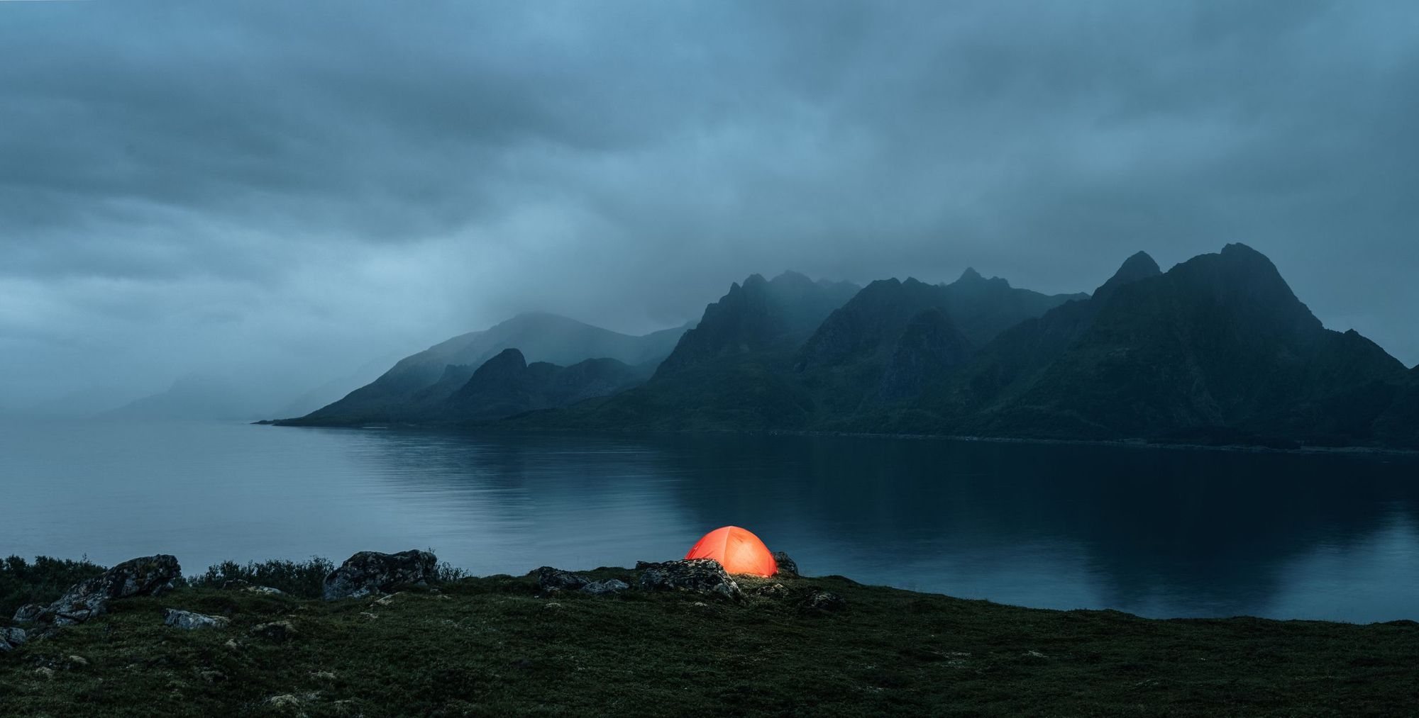 A tent lit from within, surrounded by a cloudy landscape on the Lofoten Islands, Norway.