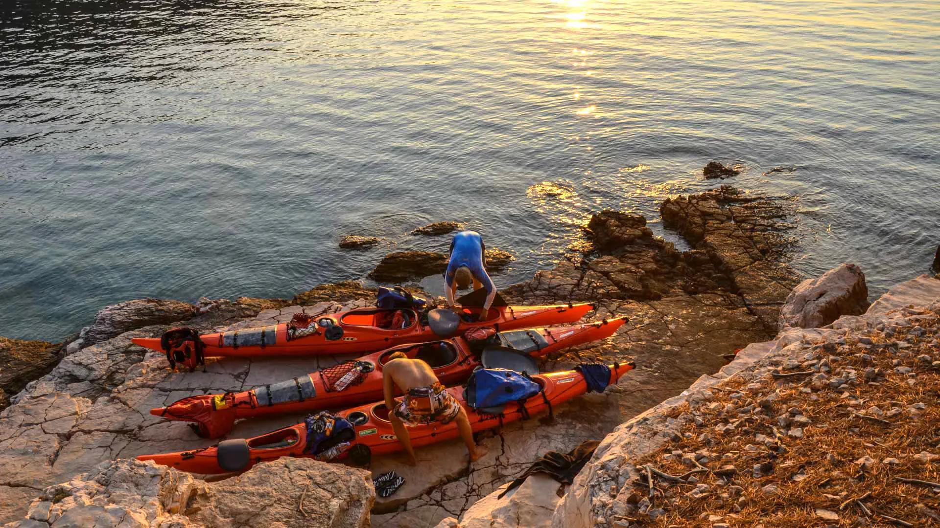 People with kayaks on land next to the sea