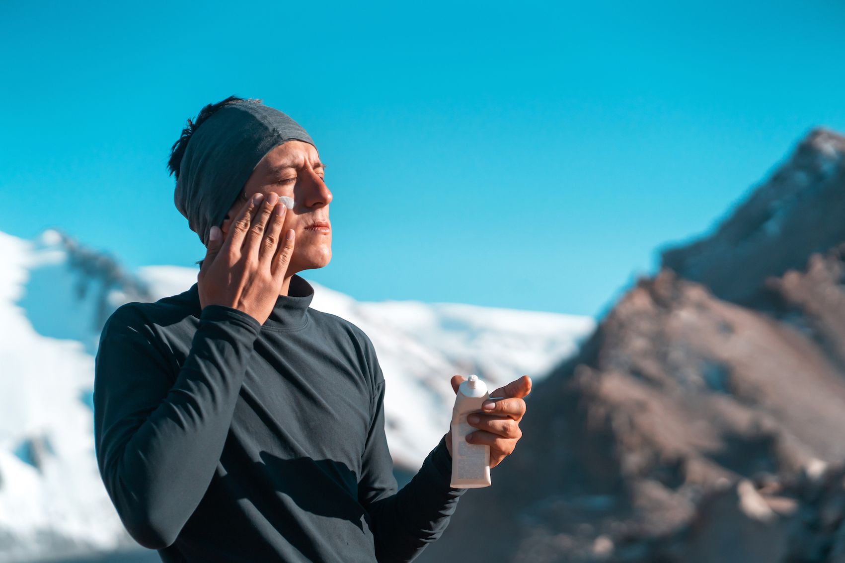 A man applying suncream with snowy mountains in the background, on a sunny day.