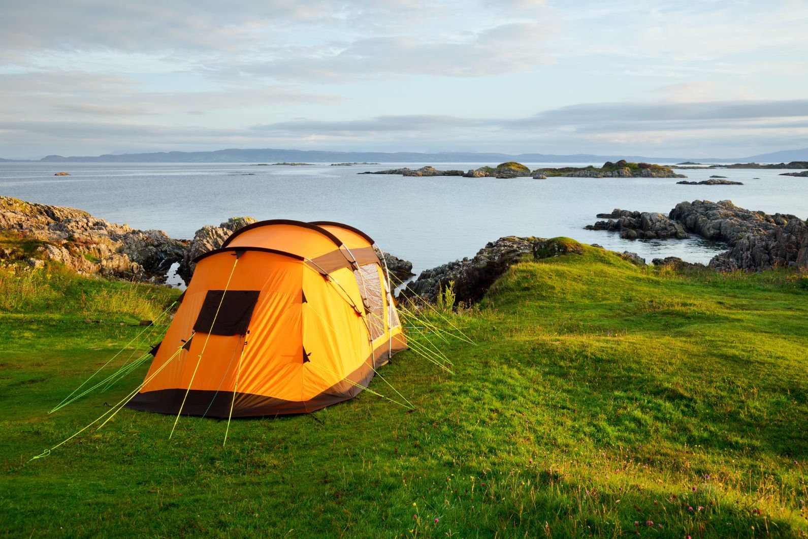 A yellow tent with guy ropes pegged sits on the edge of the Scottish coast.