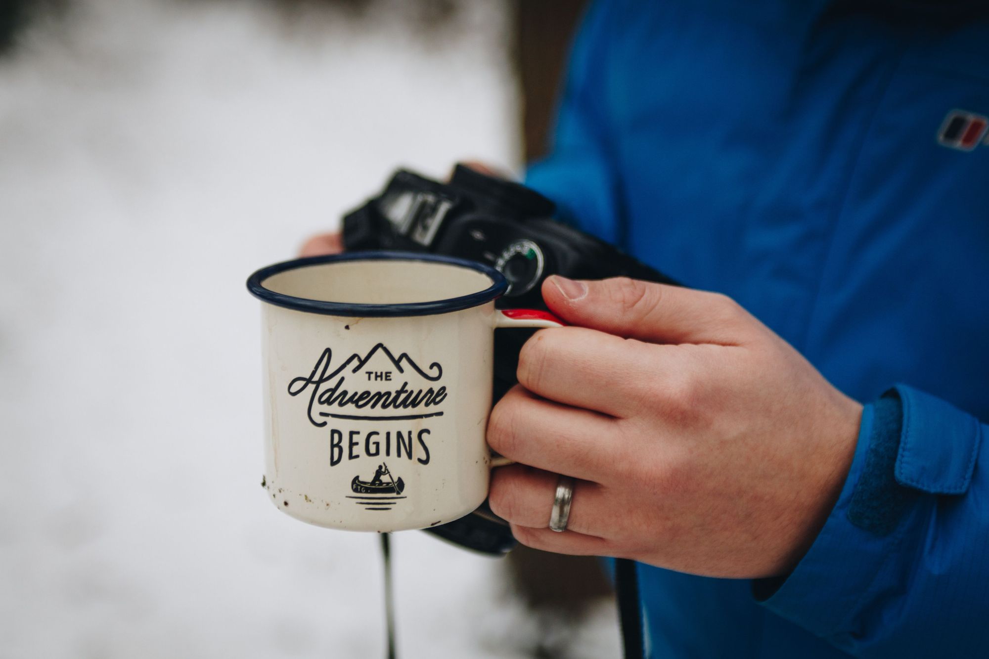 An instagram-friendly picture of a mug which reads 'The Adventure Begins' while a hiker looks into their camera.
