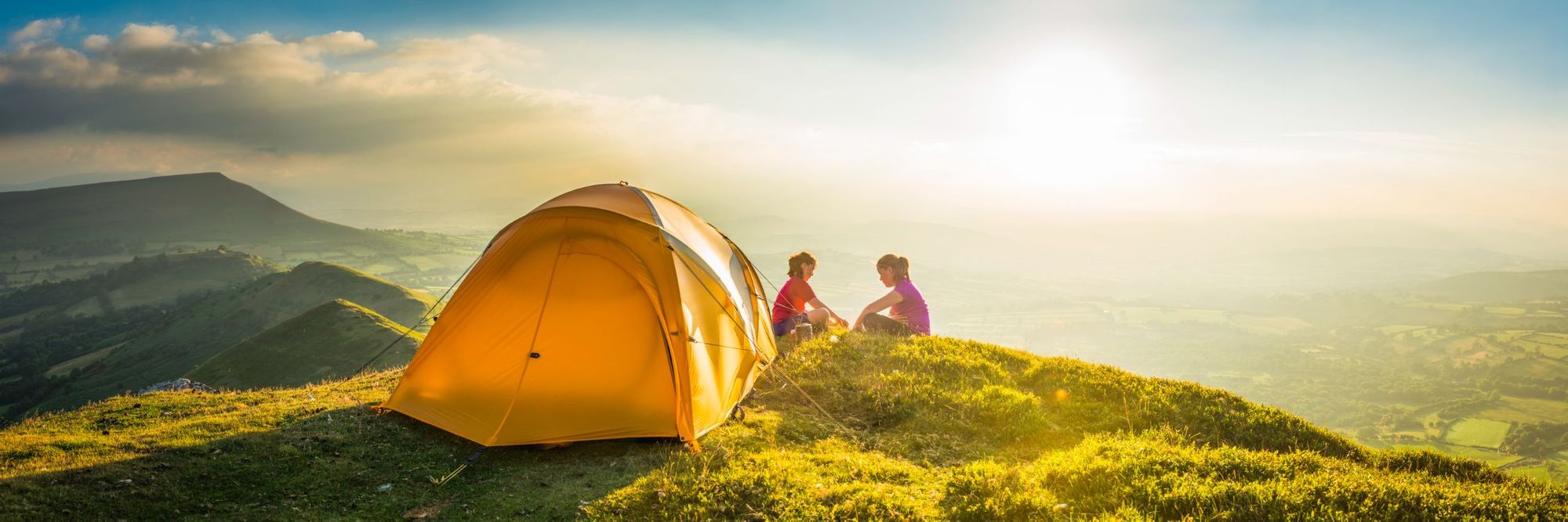 Two wild campers sit, gazing out over their view after pitching their tent.