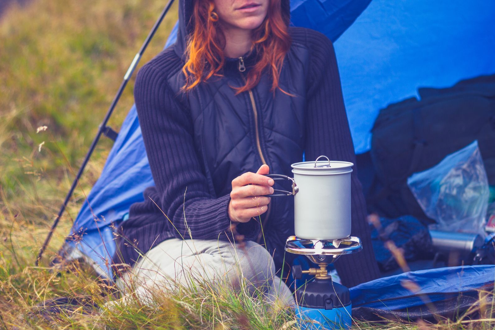 A woman relaxing next to a camping stove.