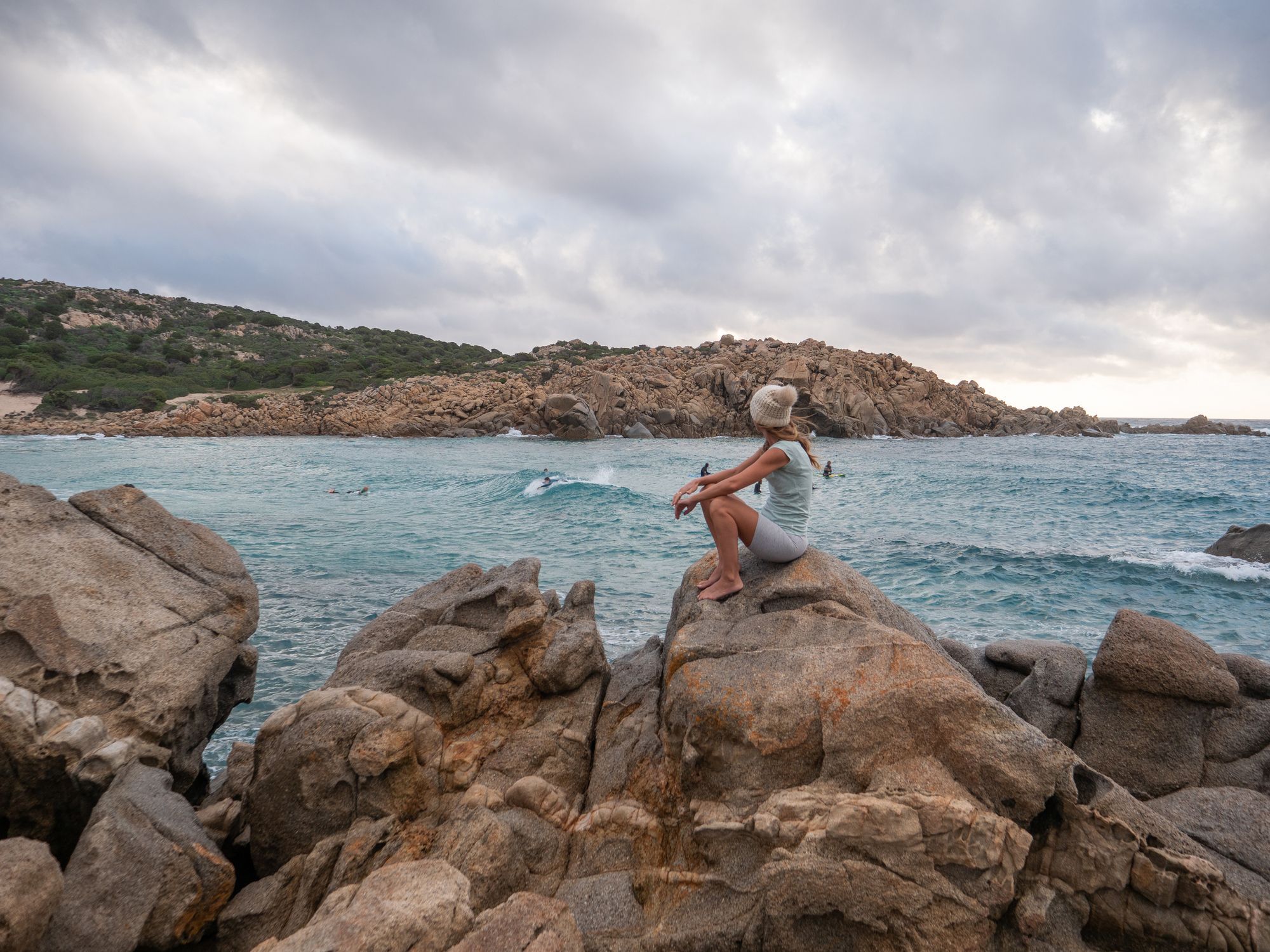 Woman watching the ocean, surfers catching waves in the background.