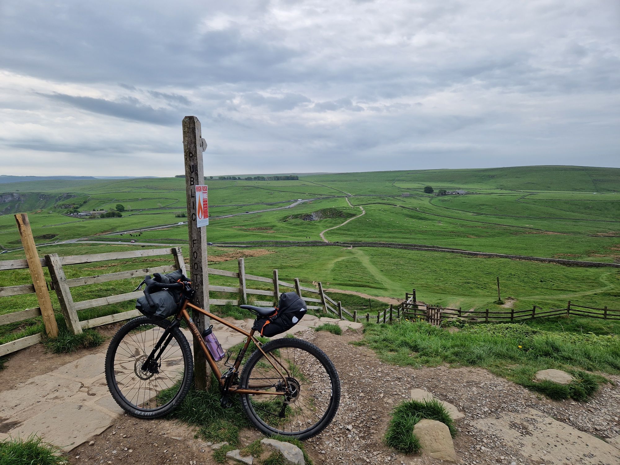 A packed bike leaning against a signpost on the path to Mam Tor.